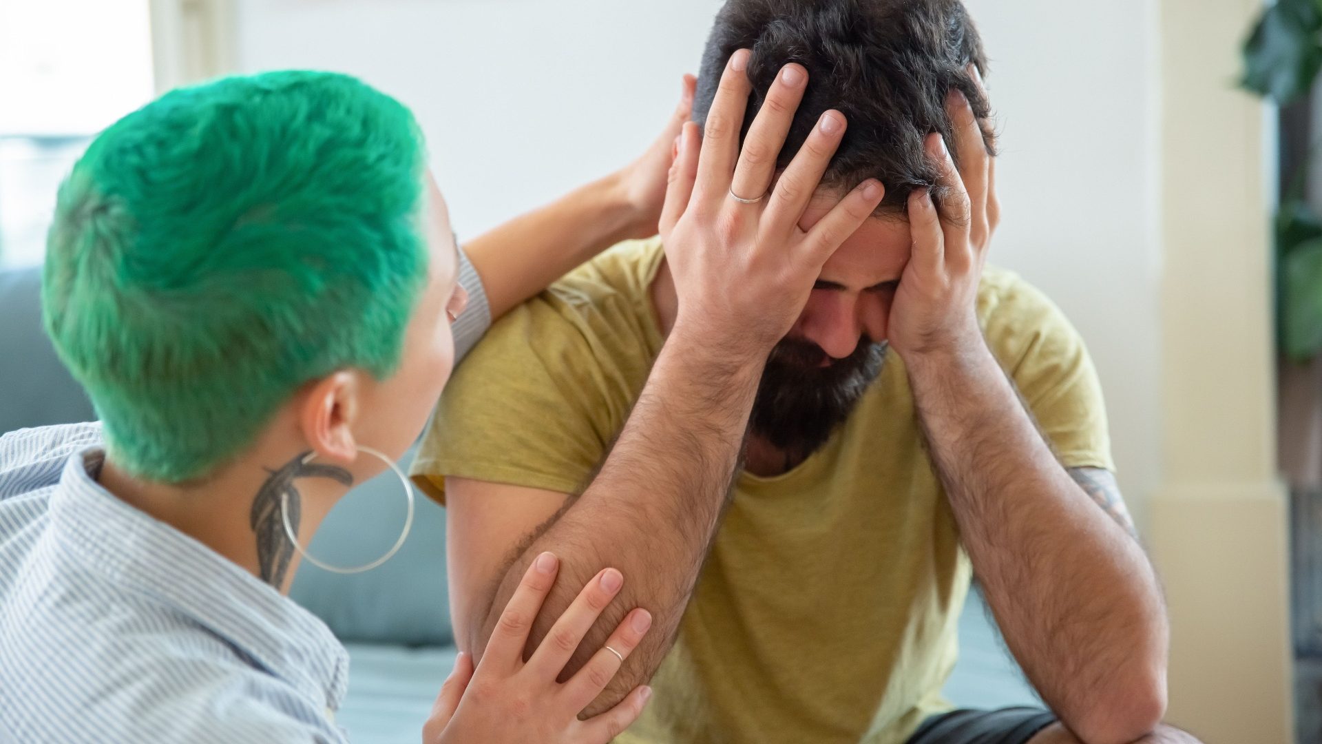A carer gently comforting and reassuring a distressed man during a moment of sensory overload at home
